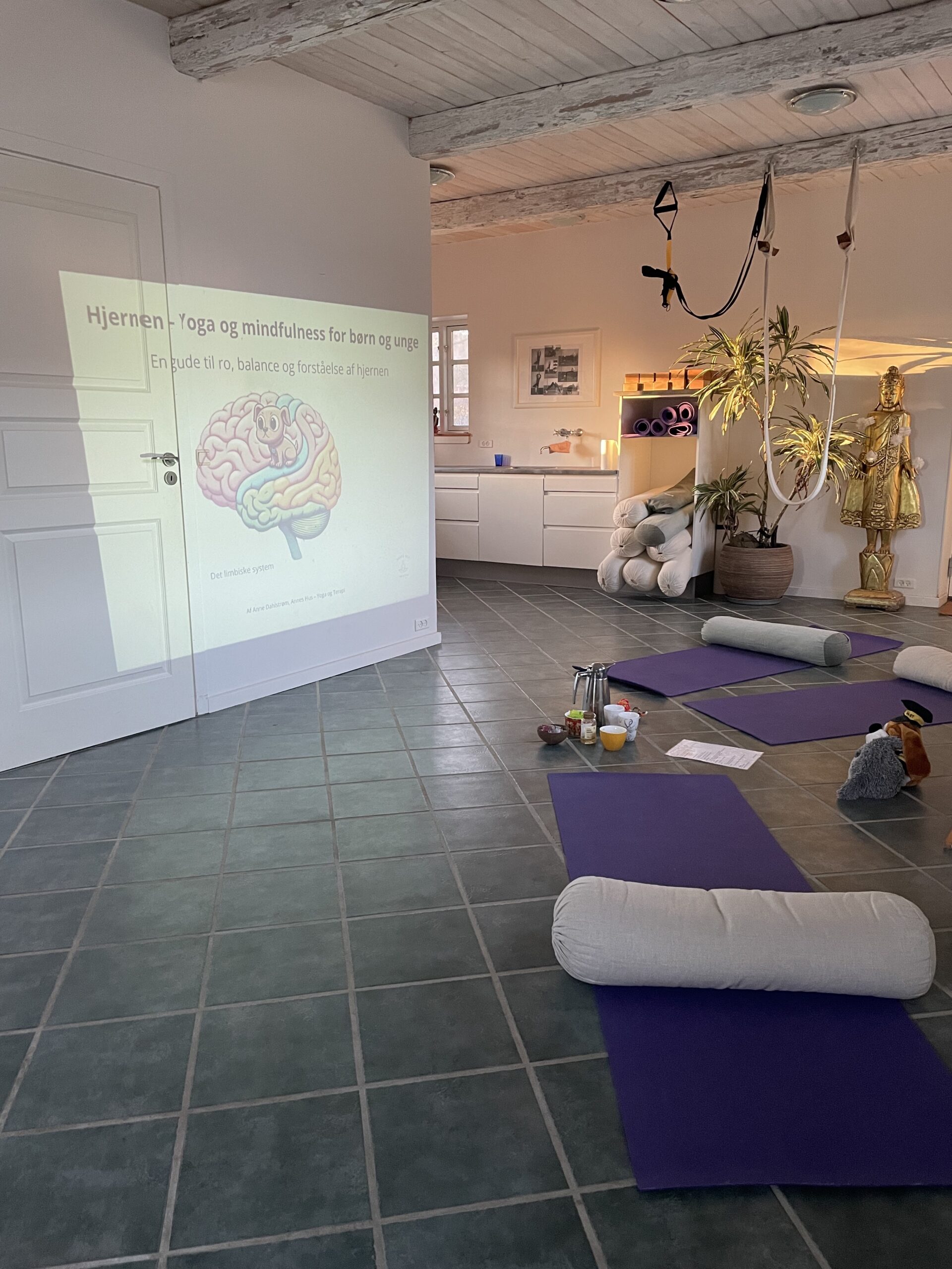 Praksisrum med yogamåtter og en præsentation projiceret på væggen under et familieforløb.